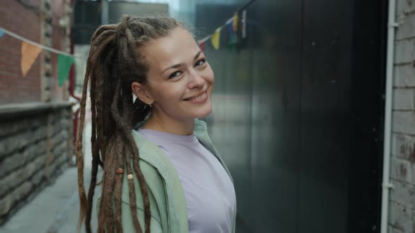Portrait of Goodlooking Young Lady with Dreadlocks Turning to Camera and Smiling Outside in City alt