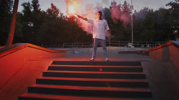 Young Fellow is Holding Glowing Red Signal Flare and Going to Perform Breakdance Standing on Stairs alt
