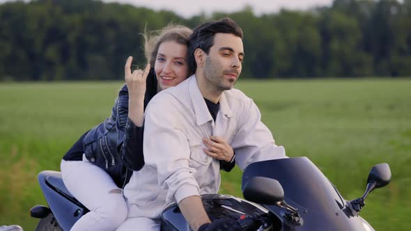 Beautiful Couple Rides Sport Motorcycle on the Road Near Summer Field