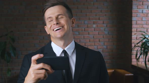 Portrait of Young Businessman Man Watching Funny Videos on a Smartphone in a Modern Office