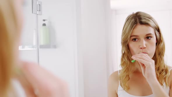 Woman looking in mirror while brushing her teeth in bathroom alt