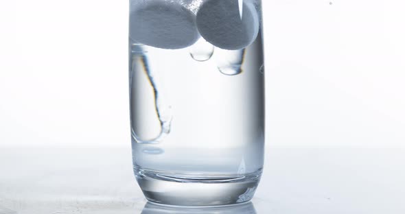 900066 Tablets Falling and Dissolving into a Glass of Water against White Background, Slow Motion 4K alt