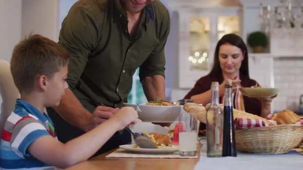 Smiling caucasian father standing at table serving son food before family meal alt