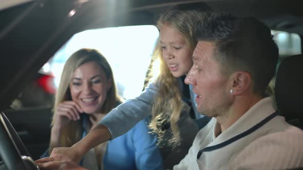 Happy Father Showing Car Dashboard to Curios Cute Daughter with Blurred Mother Smiling at Background alt