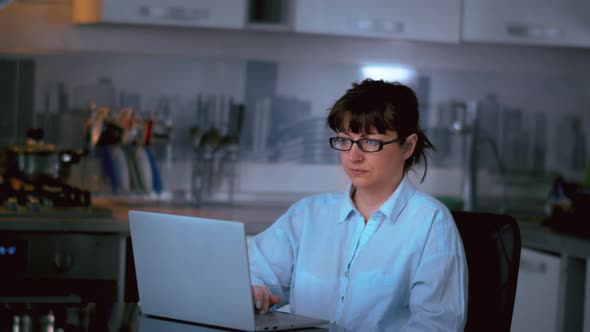 Woman Sits Motionlessly Near a Laptop and Reads Information Woman with Glasses Sits at a Laptop in