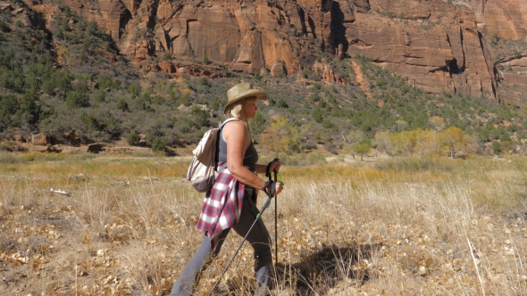 Active Woman with Trekking Sticks Hiking in Zion Park in the Background Rocks alt