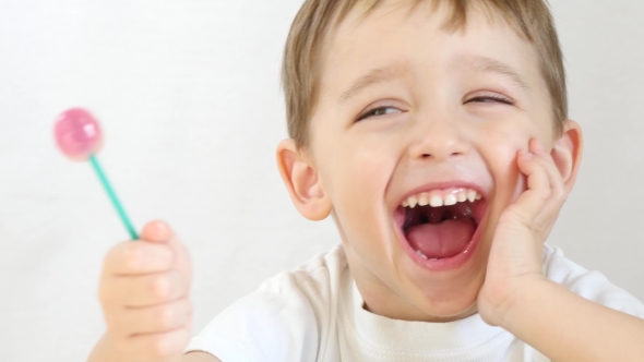 Child Happily Licks Lollipop Sitting at a Table on a White Background ...