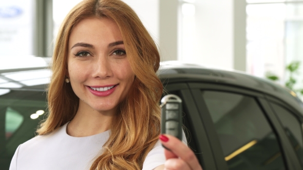 Cheerful Attractive Woman Smiling Showing Car Keys To the Camera at the Dealership alt