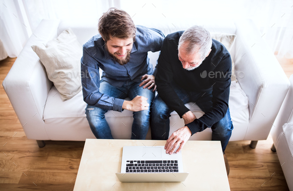Hipster son and his senior father with laptop at home. Stock Photo by halfpoint