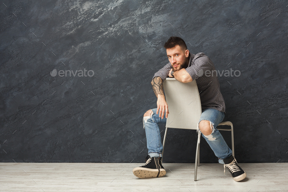 Handsome man sitting on the chair and posing in studio Stock Photo by  Prostock-studio