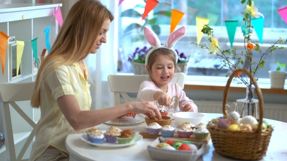Young Mother and Her Little Daughter with Rabbit Ears Cooking Easter Cupcakes alt