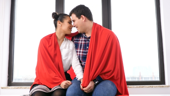 Romantic Couple Covered with a Blanket Next To a Big Window alt