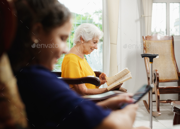 Granddaughter Using Mobile Phone And Grandma Reading Book