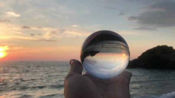 hand holding crystal ball against seaside beach view on sunset
