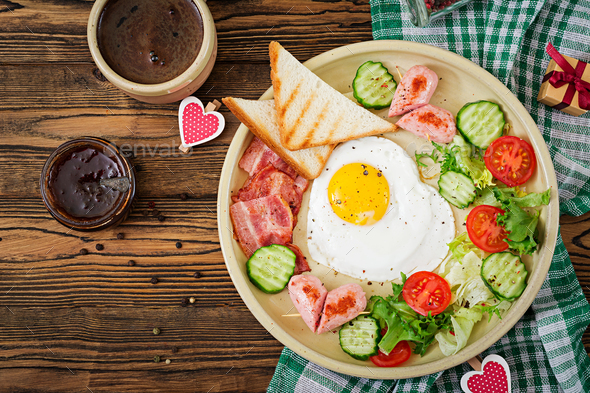 Breakfast on Valentine\'s Day - fried egg in the shape of a heart, toasts, sausage Stock Photo by Timolina