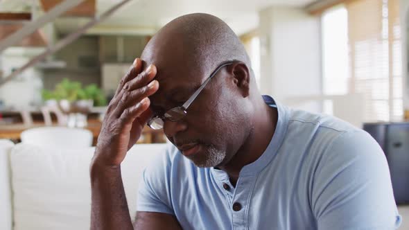 African american senior man sitting on a couch rubbing his forehead in thought alt