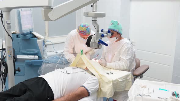 Two Female Surgeons Perform Eye Surgery with Microscope and Medical Instruments alt