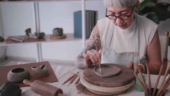 Asian elderly woman enjoying pottery work at home. alt