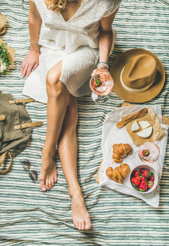 Woman in dress sitting on blanket with wine and snacks - Stock Photo - Images