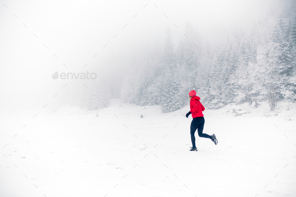 Girl trail running on snow in winter mountains