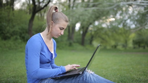 Young Girl Is Using Laptop Sitting On The Grass In The Park