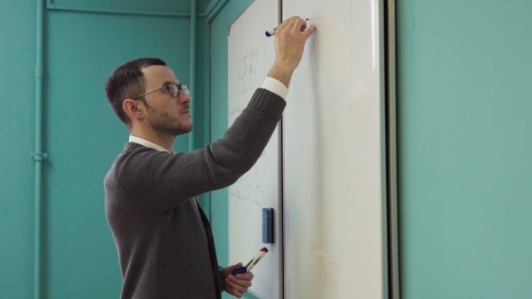 Young Male Lecturer Writes on the Whiteboard in Classroom