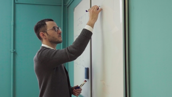 Young Male Lecturer Writes on the Whiteboard in Classroom alt