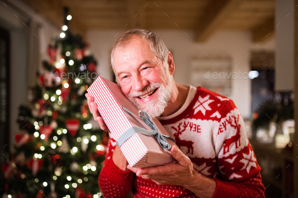 Senior man in front of Christmas tree holding a gift. Stock Photo by halfpoint