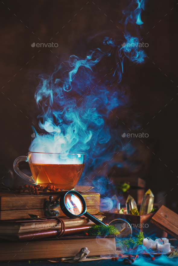 Hot cup of tea with a dense rising steam, magnifying glass, books and dried plants - Stock Photo - Images