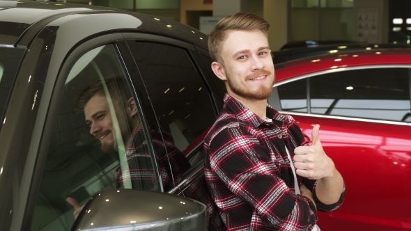 Handsome Man Showing Thumbs Up Leaning on a New Car at the Dealership alt