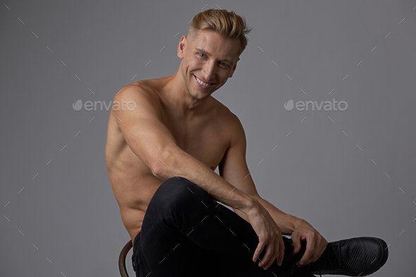 Attractive young man posing with naked torso sitting on a chair