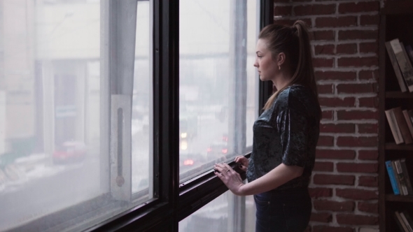 Sad Woman Goes to the Window and Looks at the City Street alt