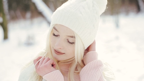 Young Attractive Blond Girl in a White Cap with a Warm Blanket on Her Shoulders in the Winter Forest