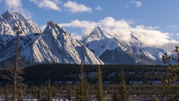 of Clouds Above Snowy Mountain Peaks and Green Forest alt