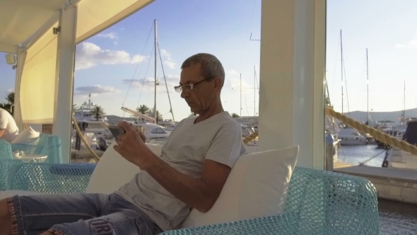 Man Sitting in a Cafe in the Marina and Using His Phone