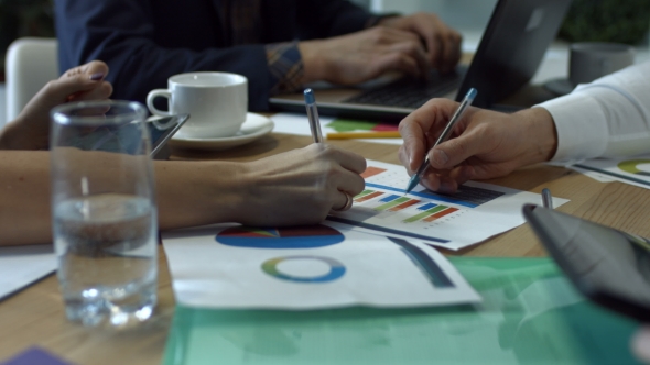 Hands Writing on Various Financial Charts on Table alt