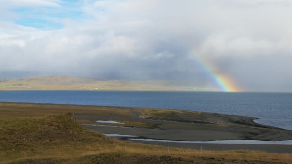 Beautiful Rainbow Over Icelandic Fjord in Sunny Day, Low Rainy Clouds and Sunshine