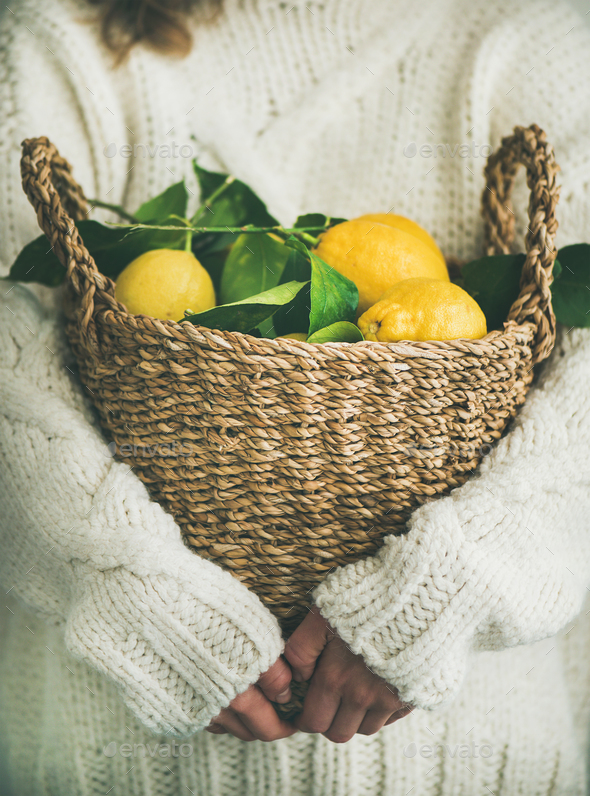 Woman in white woolen sweater holding basket of fresh lemons - Stock Photo - Images