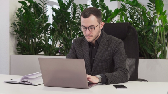 Confident Businessman with Glasses Using a Laptop in Office