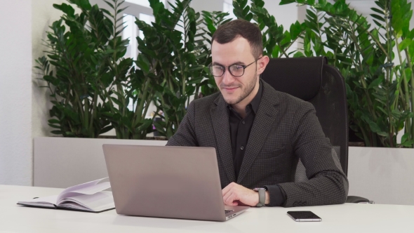 Happy Business Man with Glasses Looks at the Laptop Screen