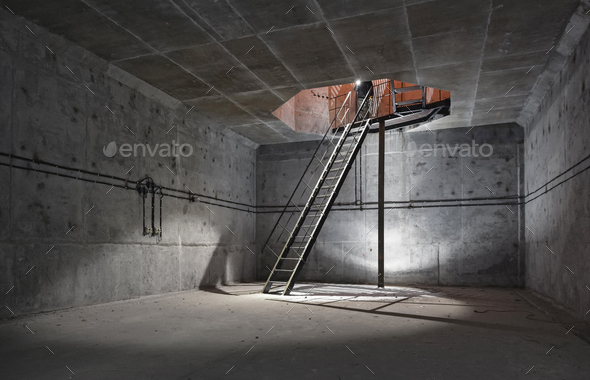 Concrete room underground with a ladder to the surface from which the light comes