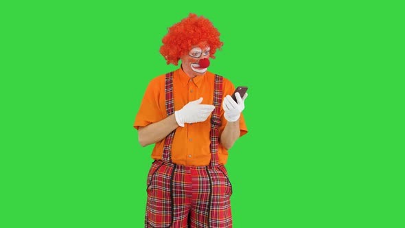 Funny Clown Looking at Smartphone and Reacting on What He Sees on a Green Screen Chroma Key alt