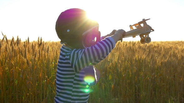 Happy Child Playing with a Toy Airplane at Sunset in a Wheat Field alt