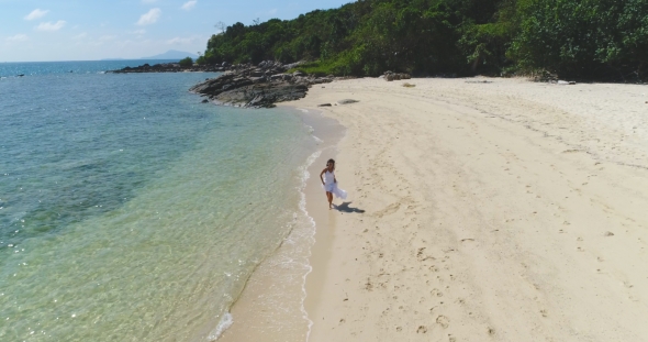 Aerial: A Girl in a White Dress Is Runing Along the Beach By the Water.
