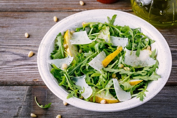 Download green salad bowl of arugula with pear, parmesan cheese and pine nuts Stock Photo by nblxer