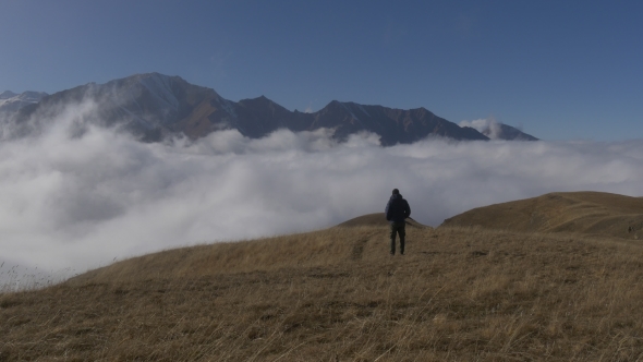 Man Stands on a Mountain Above the Clouds