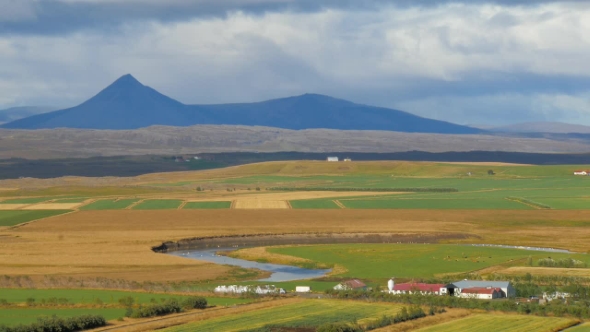 Rural Suburban Landscape in Iceland in Sunny Autumn Day, Calm River, Mountains, Agricultural Fields
