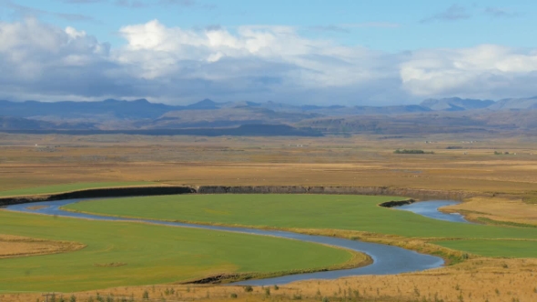 Meandering River Is Flowing Through Large Flat Field Near Mountain Range in Iceland