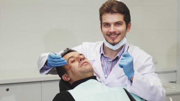 Young Male Dentist Smiling During Dental Checkup of His Patient alt