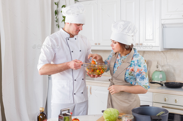 Cook in uniform and his apprentice cooking vegetarian meal